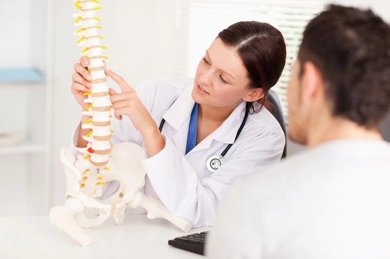 پزشک زن در حال توضیح موضوعی به بیمار با استفاده از مدل پلاستیکی ستونفقرات