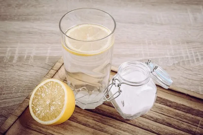 یک لیوان آب با تکه لیمو، کنار آن نمک‌پاش و نصف لیموی برش‌خورده، برای تهیه محلول الکترولیتی طبیعی. 
