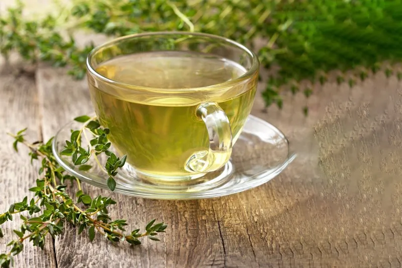 فنجان چای آویشن کنار گیاه آن، قابل استفاده برای پاکسازی ریه‌ها و دستگاه گوارش با این گیاه گرم و خشک 