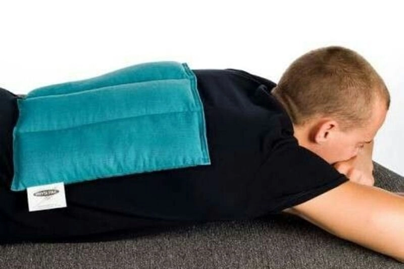 مردی روی شکم دراز کشیده و از کیسه آب گرم استفاده میکند