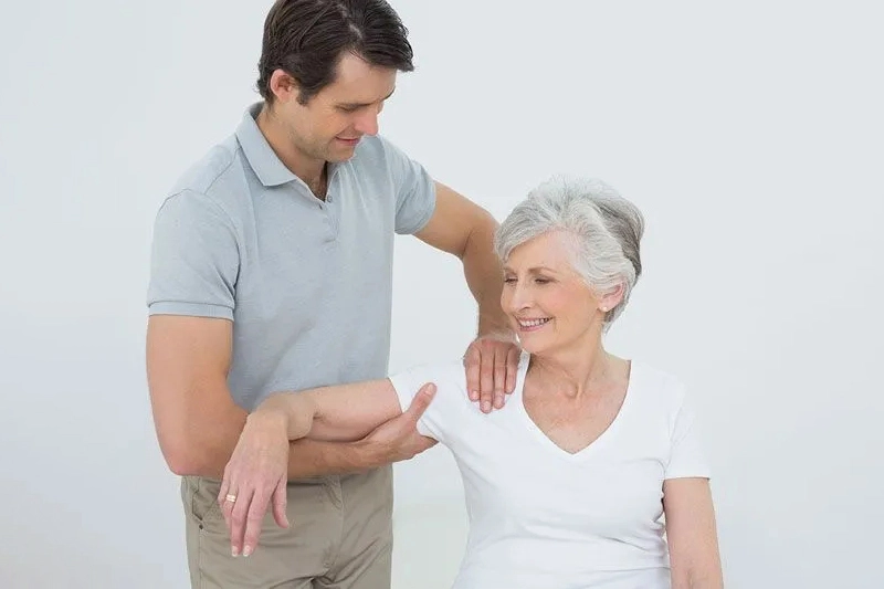 زن سالخورده روی تخت کایروپراکتیک نشسته و درمان دستی برای مدیریت کمردرد یائسگی دریافت میکند