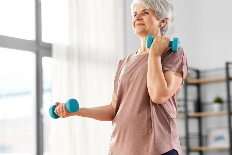 زن سالخورده در حال انجام ورزش تقویتی با وزنه سبک برای تقویت عضلات مرکزی و حمایت ستون فقرات