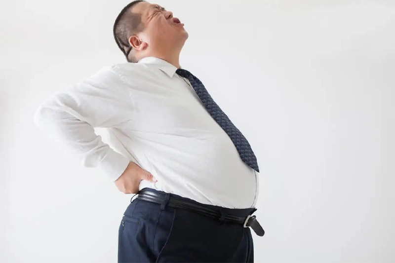 مرد چاق دستهایش را روی کمر گرفته و دچار کمردرد ناشی از اضافه وزن است