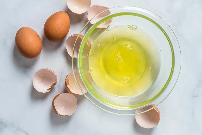 تعدادی تخممرغ شکسته در یک کاسه شیشهای آماده برای ماسک حنا و تخممرغ