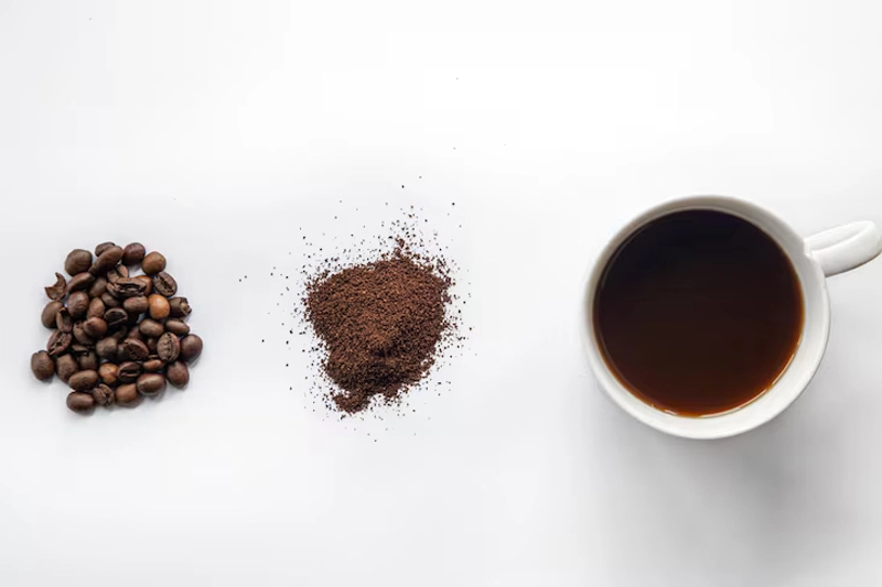 دانههای قهوه و پودر قهوه کنار یک فنجان قهوه آماده برای ماسک حنا و قهوه