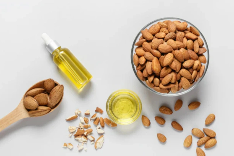 چند عدد بادام در کاسه و یک بطری روغن بادام شیرین آماده برای استفاده روی مو