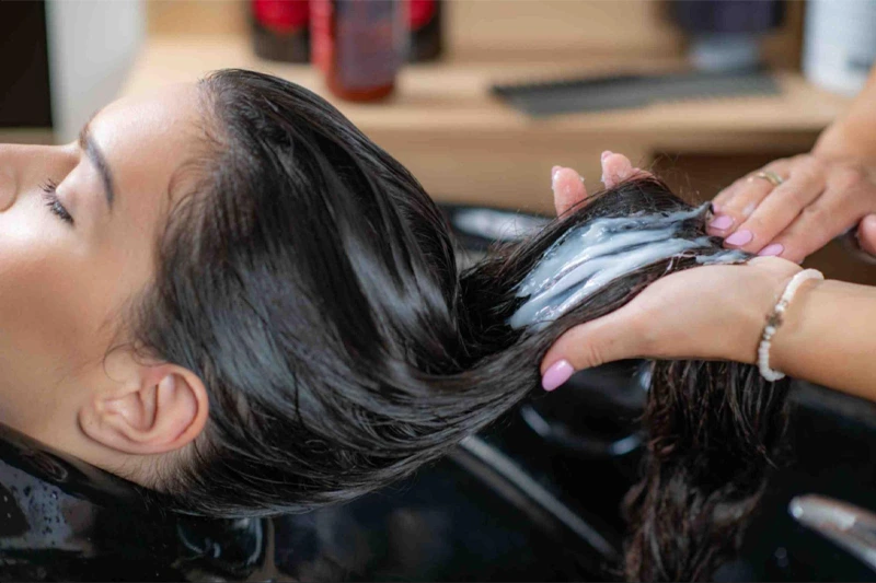 زن روی صندلی آرایشگاه نشسته و در حال دریافت ماسک موی بابونه است. 