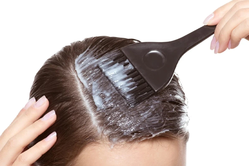 زنی که با برس ماسکهای خانگی حاوی روغن بادام را روی موهایش میمالد