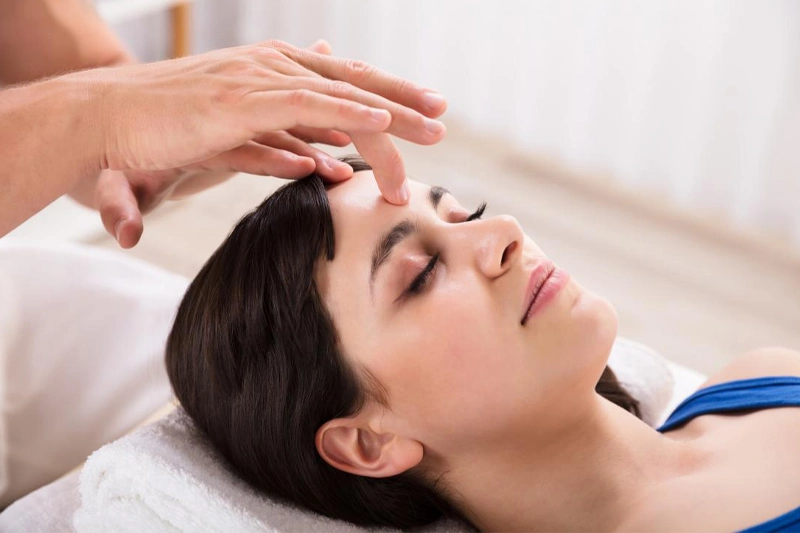 زن دراز کشیده در حال دریافت ماساژ روی پیشانی در نقطه چشم سوم برای آرامسازی ذهن و کاهش فشار سینوسها