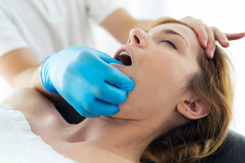 زن دراز کشیده در حال دریافت ماساژ فک با فشار ملایم بین انگشتان برای کاهش تنش عضله فک